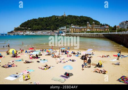 San Sebastian, Gipuzkoa, Baskenland, Spanien - 12th. Juli 2019 : die Menschen sonnen sich am Strand von La Concha in der Bucht von La Concha. Urgull Hill in Backgroun Stockfoto