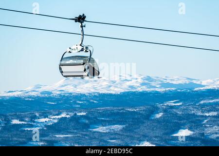 Leerer Skilift auf einer Seilbahn mit schneebedeckten Bergen im Hintergrund. Stockfoto