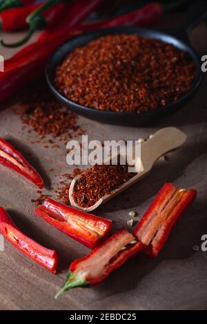 Rote frische Chili-Paprika mit grünen Schwänzen und getrocknete rote Chili-Flocken in Schüssel auf Holzbrett. Stockfoto