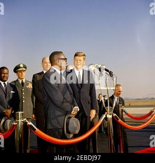 Ankunftszeremonie für William Vacanarat Shadrach Tubman, Präsident von Liberia, 10:00 UHR. Ankunftszeremonien für William V.S. Tubman, Präsident von Liberia. Auf Plattform, erste Reihe (L u2013 R): Präsident Tubman (an Mikrofonen); Präsident John F. Kennedy. Zweite Reihe: Vorsitzender der Generalstabschefs Lyman Lemnitzer; Staatssekretär Dean Rusk. Chef des Protokolls Angier Biddle Duke (rechts von der Plattform). Andrews Air Force Base, Maryland. Stockfoto