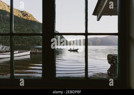 Blick auf den See und das Boot aus dem rustikalen Hüttenfenster Am frühen Morgen Stockfoto