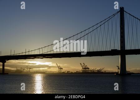 Die Sonne geht hinter der San Francisco-Oakland Bay Bridge Eastern Span auf Und über dem Hafen von Oakland Stockfoto