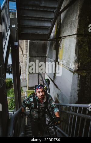 Ein hübscher junger Mann trägt sein Fahrrad auf der Schulter nach oben Die Treppe Stockfoto