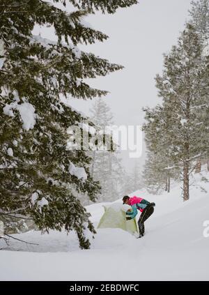 Ein Mann in heller Jacke steht draußen Zelt in der Tiefe Schnee Stockfoto