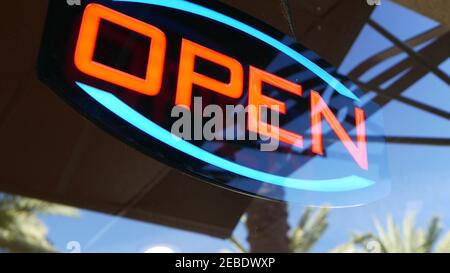 Offenes Neonschild, das im Dunkeln leuchtet. Lebendiger Text im Retro-Stil am Eingang am Glasfenster. Bunte elektrische Banner selektive Fokus Nahaufnahme. Glühlampe Stockfoto