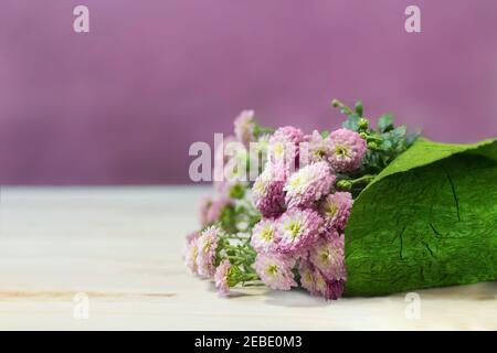 Blumenstrauß in grünem Geschenkpapier. Kleine weiße und rosa Chrysanthemen auf dem Tisch. Anwesend. Speicherplatz kopieren Stockfoto