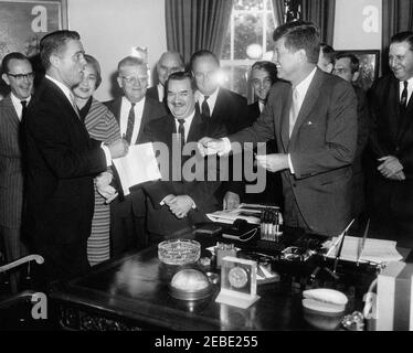 Bill Signing - H.R. 7500 Öffentliches Recht 87-293, Peace Corps Act, 9:45am. Präsident John F. Kennedy reicht dem Direktor des Friedenskorps R. Sargent Shriver einen Stift, nachdem er HR 7500, das Friedenskorps-Gesetz, im Oval Office, im Weißen Haus, Washington, D.C. unterzeichnet hat. Links nach rechts: Senator Philip A. Hart von Michigan; Direktor Shriver; Vertreterin Edna Kelly von New York; Vertreter Chester Merrow aus New Hampshire; Vertreter Thomas F. Johnson aus Maryland (hinten); Vertreter Clement Zablocki aus Wisconsin; Vertreter Wayne L. Hays aus Ohio; Vertreter Roman C. Pucinski aus Illinois; Präsident Ken Stockfoto