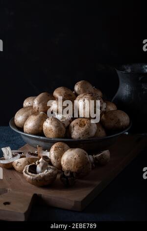 Frische Champignon (Knopf) Pilze in Schüssel auf einem Holzbrett vor dem dunklen Hintergrund. Stockfoto