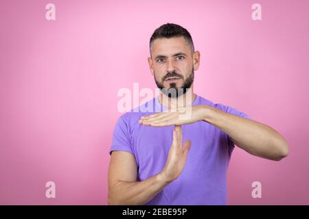 Junger schöner Mann trägt lässiges T-Shirt über rosa Hintergrund tun Auszeit Geste mit Händen, frustriert und ernstes Gesicht Stockfoto