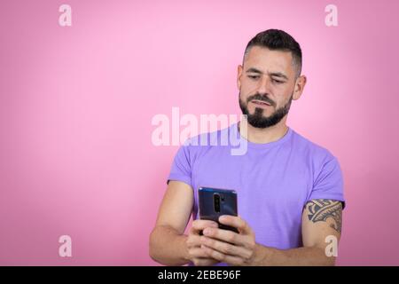 Junger schöner Mann trägt lässiges T-Shirt über rosa Hintergrund Texting Mit ihrem Telefon Stockfoto