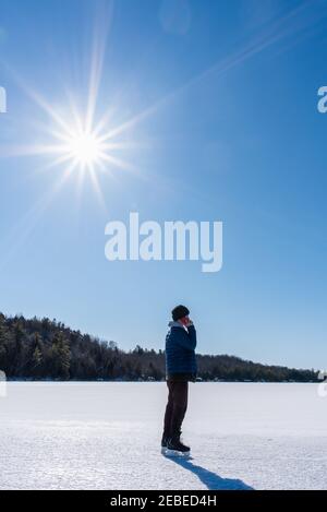 Teenager Junge auf Smartphone und Schlittschuhe auf einem gefrorenen See an einem Wintertag. Stockfoto