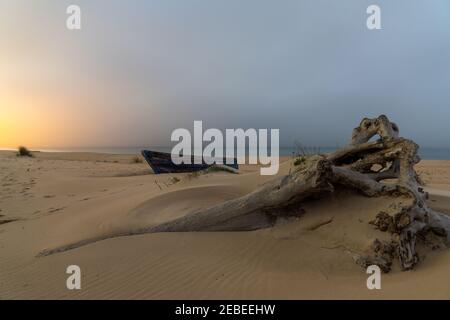 Ein altes Fischerboot aus Holz und Treibholz am Strand Nach Sonnenuntergang mit Dorflichtern dahinter Stockfoto