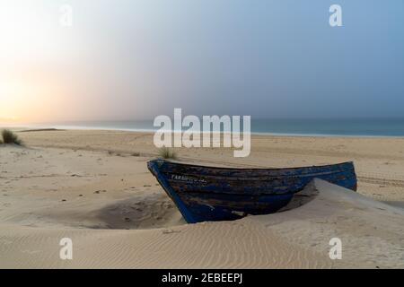 Ein buntes altes hölzernes Ruderboot, das im Sand vergraben ist Ein Strand nach Sonnenuntergang mit buntem Himmel Stockfoto
