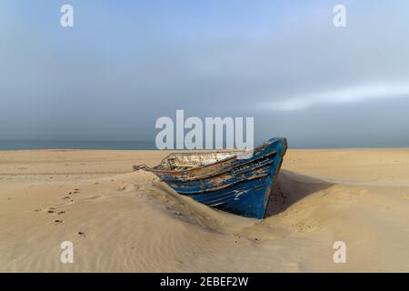 Ein buntes altes hölzernes Ruderboot, das im Sand vergraben ist Ein Strand nach Sonnenuntergang mit buntem Himmel Stockfoto