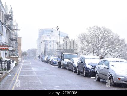 Blick auf die Straße mit Autos, Bäumen und schneebedeckten Gebäuden in England. Stockfoto