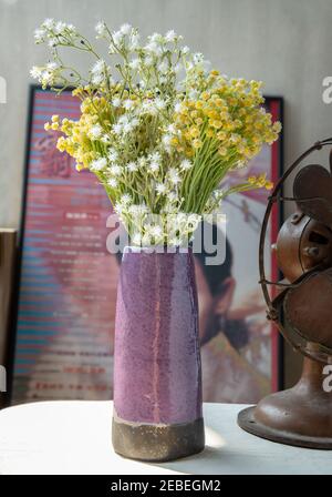 Blumenstrauß in lila Keramik Vase auf weißem texturierten Tischtuch vor dem klassischen chinesischen Plakat Film Rahmen mit alten Zement Wand. Home Deco Stockfoto