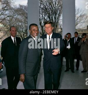 Mittagessen zu Ehren von Sylvanus Olympio, Präsident von Togo, 1:00pm Uhr. Präsident John F. Kennedy besucht mit Präsident von Togo, Sylvanus Olympio (links), nach der Ankunft von Präsident Olympiou2019s im Weißen Haus für ein Mittagessen zu seinen Ehren. Ganz links steht der Chef des Protokolls, Angier Biddle Duke; rechts im Hintergrund stehen Fotografen, darunter der Nachrichtenfotograf von United Press Movietone, Thomas J. Craven, Sr., und der Filmfotograf von Columbia Broadcasting System (CBS), Tom J. Craven, Jr.. North Portico, White House, Washington, D.C. Stockfoto