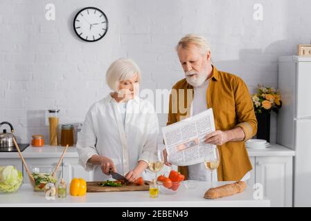 Ältere Ehepaare lesen Zeitung während sie Salat kochen Stockfoto