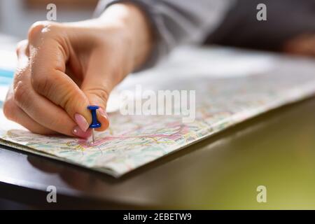 Weibliche Hand hält den Stift, der die Position eines Zielpunkts auf einer Karte anzeigt. Reiseziel, PIN auf der Karte. Selektiver Fokus. Blauer Stecknadel Stockfoto