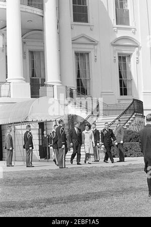 First Lady Jacqueline Kennedyu0027s (JBK) Musikprogramm für Jugendliche, 2:35pm. Präsident John F. Kennedy und First Lady Jacqueline Kennedy gehen vom Südportikus zum Südlawn des Weißen Hauses, um an der dritten Serie von Musikprogrammen für Jugendliche von Kennedyu0027s teilzunehmen. Mehrere nicht identifizierte soziale Helfer flankieren Präsident Kennedy und die First Lady. Washington, D.C. Stockfoto