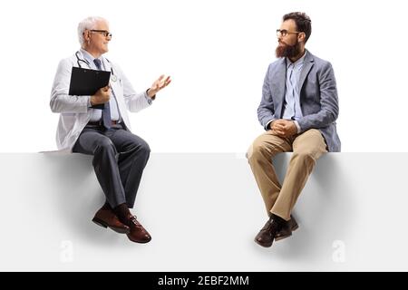 Reifer Arzt sitzt auf einer leeren Tafel mit einem Gespräch Mit einem bärtigen Mann isoliert auf weißem Hintergrund Stockfoto