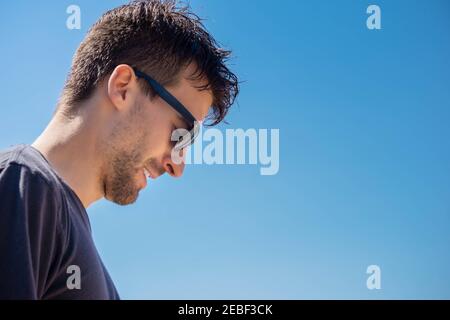 Porträt eines Mannes mit Sonnenbrille neigte seinen Kopf auf Himmel Hintergrund. Schüchterner Kerl im Sonnenbrillen-Portrait. Profil von stilvollen Mann in schwarzem Hemd und Brille Stockfoto