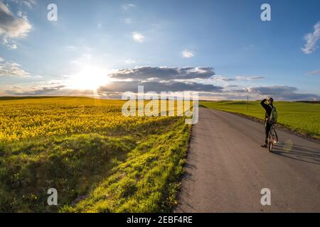 Der Radfahrer steht auf der Straße und schaut in die Entfernung und bewundert die schöne Landschaft bei Sonnenuntergang Stockfoto