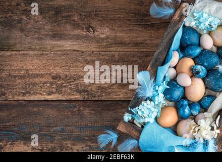 Osterhintergrund mit marmorblau und pastellfarbenen Wachteln und Hühnereiern, dekoriert mit blauen Federn und Blumen Stockfoto