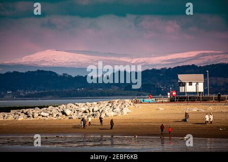 Morecambe, Lancashire, Großbritannien. Februar 2021, 10th. Ein weiterer kalter, aber heller Tag mit Familien, die sich warm am Strand mit Schnee auf den umliegenden Hügeln einhüllen Credit: PN News/Alamy Live News Stockfoto