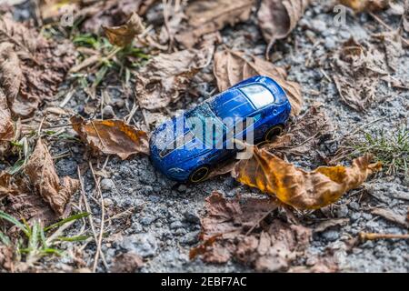 Ein blaues kleines Spielzeugauto liegt auf dem Boden bedeckt Mit Schmutz und Sand umgeben von heruntergefallenen Blättern links und Vergessen entlang der Strecke in einem Park auf einer Sonne Stockfoto