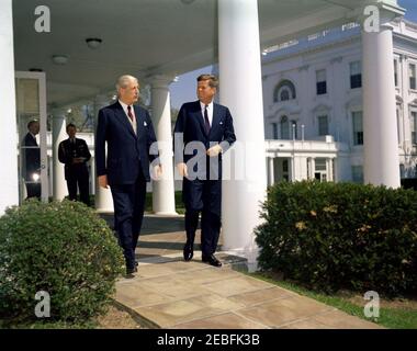 Treffen mit Harold Macmillan, Premierminister von Großbritannien, 10:57AM Uhr. Präsident John F. Kennedy geht mit Premierminister von Großbritannien Harold Macmillan in der West Wing Colonnade, im Weißen Haus, Washington, D.C. vorbei der britische Außenminister und Earl of Home Alec Douglas-Home geht durch eine Tür im Hintergrund; Military Aide to the President Chester V. Clifton schaut zu. Stockfoto