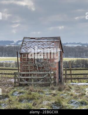 Braunston, Northamptonshire, UK - 11th. Februar 2021: Eine kleine, leicht verfallene, gemauerte Hütte mit Schnee auf dem Ziegeldach. Stockfoto