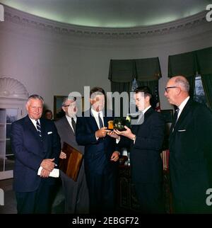 Besuch des Boysu0027 Clubsu0027 u0022Boy des Jahres,u0022 Stephen Lutz, 10:57AM. Präsident John F. Kennedy (Mitte) hält ein Modell im Maßstab, eingeschlossen in einer Flasche, von PT Boot 109, präsentiert ihm von den Boysu0027 Clubs von Americau0027s (BCA) u0022Boy der Yearu0022 Stephen Lutz von Newark, New Jersey. (L-R) Albert L. Cole, Präsident der BCA; nicht identifizierter Mann (hinten, teilweise versteckt); John M. Gleason, Nationaldirektor der BCA; Präsident Kennedy; Stephen Lutz; und Charles R. Messier, Executive Director der Boysu0027 Clubs von Newark, New Jersey. Ovales Büro, Weißes Haus, Stockfoto