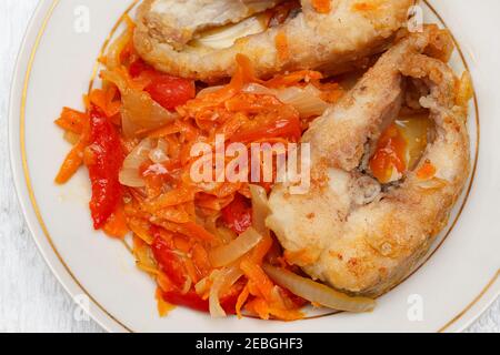 Stücke gebratener Hecht mit einer Gemüsegarnitur aus Paprika, Zwiebeln und Karotten auf einem runden weißen Teller. Lebensmittel, die reich an Eiweiß und Vitaminen. Stockfoto