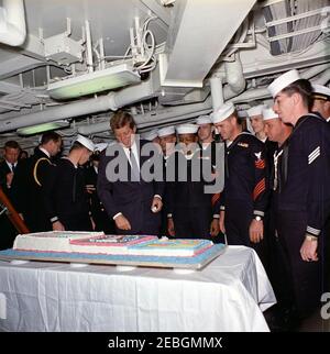 Besuch der Atlantischen Flotte: Präsentation einer Torte an Präsident Kennedy an Bord der USS Northampton (CC-1). Präsident John F. Kennedy (Mitte links) bewundert einen Kuchen, der vorbereitet wird, um seinen Besuch an Bord des Kreuzfahrtschiffes USS Northampton (CC-1), Kommandoschiff der US-Atlantikflotte, auf See vor der Küste von Virginia und North Carolina zu gedenken. Marine Aide to the President Captain Tazewell Shepard, Jr. steht links; Commissary Steward Petty Officer First Class, Horace L. Medders, USN (einer der Seeleute, die den Kuchen gebacken haben), steht vierter von rechts; Besatzungsmitglieder schauen zu. Präsident Kennedy bestieg das Schiff Stockfoto