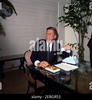 Eröffnungszeremonie für die Seattle Worldu0027s Fair von Palm Beach. Präsident John F. Kennedy (sitzt auf Terrasse Tisch) lacht während der Eröffnungsfeier für die 1962 Seattle Worldu0027s Fair (auch bekannt als die Century 21 Exposition) aus der Residenz von C. Michael Paul in Palm Beach, Florida. Präsident Kennedy hielt telefonische Bemerkungen ab und drückte eine goldene Telegrafentaste (auf dem Tisch), um die Messe per Satellitensignal von Palm Beach zu öffnen. Stockfoto