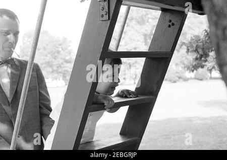 Vizepräsident Lyndon B. Johnson (LBJ) präsentiert Caroline Kennedy (CBK) ein neues Pony, u201cTexu201d; Kinder spielen auf dem South Lawn. John F. Kennedy, Jr., klettert die Leiter eines Baumhauses auf dem South Lawn of the White House, Washington, D.C. der Mann links ist nicht identifiziert. Stockfoto