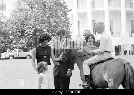 Vizepräsident Lyndon B. Johnson (LBJ) präsentiert Caroline Kennedy (CBK) ein neues Pony, u201cTexu201d; Kinder spielen auf dem South Lawn. Präsident John F. Kennedy, First Lady Jacqueline Kennedy und Caroline Kennedy besuchen mit Vizepräsident Lyndon B. Johnson und Lynda Bird Johnson den South Lawn des Weißen Hauses. Ein nicht identifizierter Junge sitzt rittlingen Tex, ein Pony an Caroline als Geschenk von Vice President Johnson gegeben. Washington, D.C. Stockfoto
