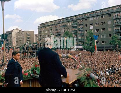 Europa-Reise: Deutschland, West-Berlin, Präsident Kennedy spricht im Rathaus Schu00f6neberg, 12:50pm Uhr. Präsident John F. Kennedy (ganz links) beobachtet als Sprecher des Berliner Abgeordnetenhauses, Otto Bach, vor einer Menschenmenge am Rudolph Wilde Platz von der Treppe des West Berlinu2019s Rathauses, Rathaus Schu00f6neberg, Rede halten. Bundesrepublik Deutschland. Stockfoto