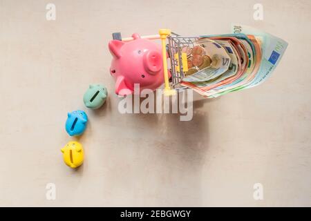 Ferkel Banken nach großen Schweinebank, die rollenden Warenkorb mit Euro-Noten auf Holz Hintergrund. Großes Schwein, kleine Schweinebänke und Euro-Banknoten in s Stockfoto