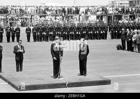 Reise nach Mexiko: Ankunftszeremonie, Internationaler Flughafen Mexiko-Stadt, Mexiko-Stadt, 11:00am Uhr. Präsident John F. Kennedy (an Mikrofonen) hält Bemerkungen bei seiner Ankunft in Mexiko-Stadt. Der Präsident von Mexiko, Adolfo Lu00f3pez Mateos, steht auf der Plattform rechts; der Dolmetscher des US-Außenministeriums, Donald Barnes, steht unter der Plattform links. Ebenfalls abgebildet: Sonderassistent des Präsidenten von Mexiko, Justo Sierra. Im Hintergrund stehen Mitglieder eines Ehrengardes. Internationaler Flughafen Benito Juu00e1rez, Mexiko-Stadt, Mexiko. Stockfoto