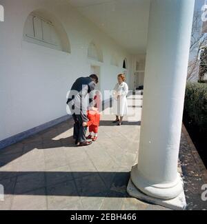 Präsident Kennedy mit John F. Kennedy, Jr. (JFK, Jr.), u0026 Caroline Kennedy (CBK). Präsident John F. Kennedy spielt mit seiner Tochter Caroline Kennedy (die zwischen ihren fatheru2019s Beinen läuft) in der Westflügel-Kolonnade des Weißen Hauses, Washington, D.C., John F. Kennedy, Jr. geht im Hintergrund; Kindermädchen zu den Kennedy-Kindern, Maud Shaw, steht rechts. Stockfoto