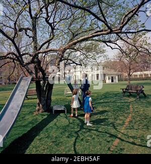 Präsident Kennedy mit Caroline Kennedy (CBK) u0026 John F. Kennedy, Jr. (JFK, Jr.), auf dem South Lawn. Präsident John F. Kennedy (Mitte rechts, weggewandt) sieht zu, wie sein Sohn John F. Kennedy, Jr., oben auf der Treppe des Baumhauses auf dem South Lawn des Weißen Hauses, Washington, D.C. steht Caroline Kennedy und Sally Fay, Tochter von Kennedys Freund und Untersekretär der Marine, Paul u0022Redu0022 Fay (in blauem Kleid), steht vor der Treppe; Kindermädchen zu den Kennedy-Kindern, Maud Shaw (hinten, mit Sonnenbrille), schaut auf. Der Westflügel des Weißen Hou Stockfoto