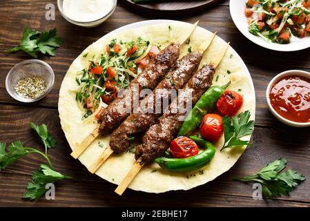Türkischer Adana Kebab mit frischem Gemüse auf Fladenbrot über Holztisch. Leckeres Essen im arabischen Stil. Nahaufnahme Stockfoto