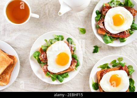 Offene Sandwiches mit Spiegeleiern, Speck und Gemüseblättern auf hellem Hintergrund. Draufsicht, flach liegend Stockfoto