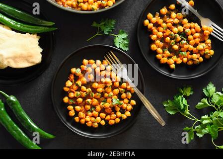 Knusprig geröstete Kichererbsen im indischen Stil auf schwarzem Steingrund. Vegetarisches veganes Food Konzept. Draufsicht, flaches Lay Stockfoto