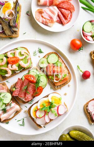 Offene Sandwiches mit Fleisch, Gemüse und Meeresfrüchten auf dem Teller auf hellem Steingrund. Draufsicht, flach liegend. Stockfoto