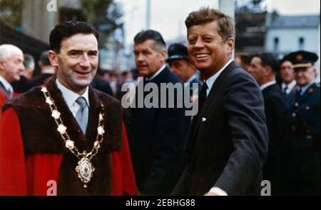 Europareise: Irland, Galway: Präsident Kennedy am Eyre Square, Bemerkungen und Abreise, 11:55am Uhr. Präsident John F. Kennedy und der Bürgermeister von Galway, Alderman Patrick D. Ryan (links), kommen am Eyre Square in Galway, Irland, vor einer Begrüßungszeremonie zu Ehren von Präsident Kennedy an. Ebenfalls im Bild: Geheimagent des Weißen Hauses, Gerald u201cJerryu201d Behn (hinten Mitte) und Air Force Aide to President Kennedy, Brigadier General Godfrey T. McHugh (teilweise versteckt hinter Behn). Stockfoto