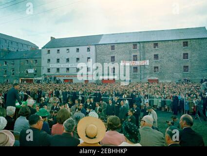 Europareise: Irland, New Ross. Präsident John F. Kennedy (links, am Rednerpult) hält eine Rede vor der Menschenmenge, die sich am New Ross Quay in New Ross, County Wexford, Irland, versammelt, dem Hafen, von dem sein Urgroßvater, Patrick Kennedy, in die Vereinigten Staaten emigrierte. Reporter und Fotografen beobachten von unten speakersu0027 Plattform; auch im Bild (sitzt auf speakersu0027 Plattform): Stellvertretender Vorsitzender des New Ross Urban District Council, Gerald Donovan; Präsident Kennedyu0027s Schwester, Jean Kennedy Smith; die Presidentu0027s Schwägerin, Prinzessin Lee Radziwill von Polen; Präsident o Stockfoto