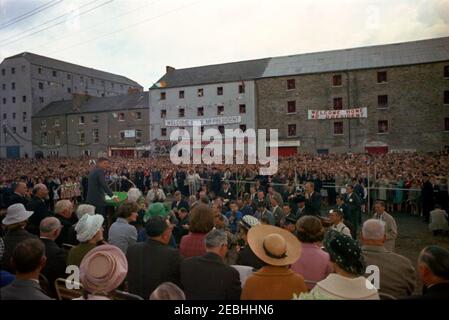 Europareise: Irland, New Ross. Präsident John F. Kennedy (links, am Rednerpult) hält eine Rede vor der Menschenmenge, die sich am New Ross Quay in New Ross, County Wexford, Irland, versammelt hat, dem Hafen, von dem sein Urgroßvater, Patrick Kennedy, in die Vereinigten Staaten emigrierte. Reporter und Fotografen beobachten von unten speakersu0027 Plattform; auch im Bild (sitzt auf speakersu0027 Plattform): Minister für auswärtige Angelegenheiten von Irland, Frank Aiken; Vorsitzender des New Ross Urban District Council, Andrew Minihan; Vice Chairman des New Ross Urban District Council, Gerald Donovan; Präsident Ken Stockfoto